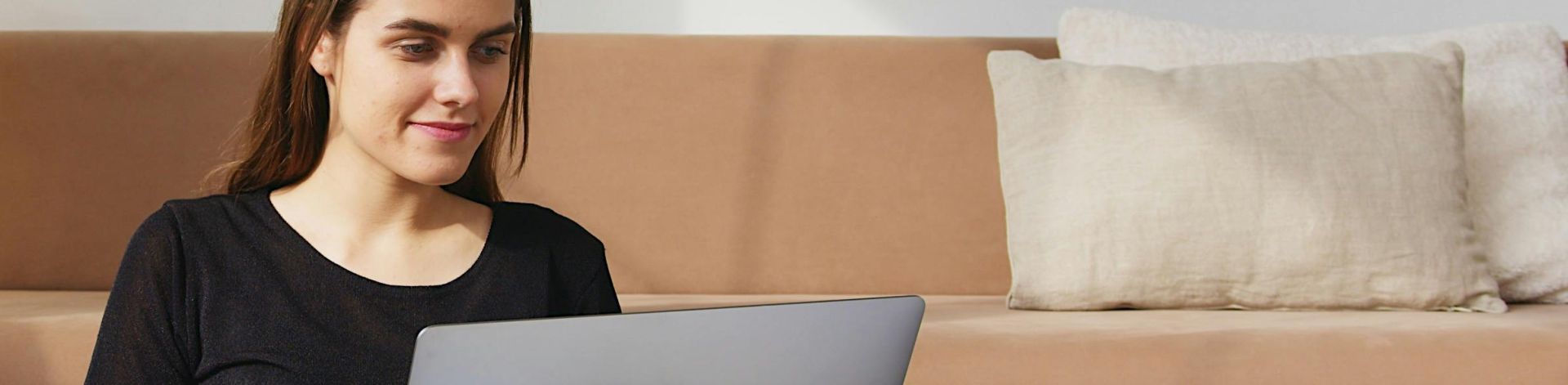 A young woman sitting comfortably on a sofa with a laptop in a cozy living room environment.